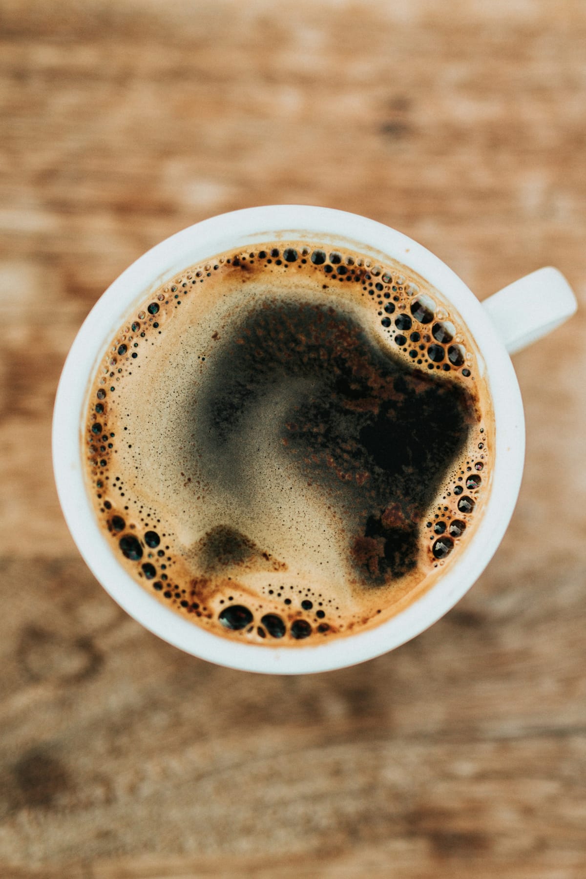 A cup of black coffee on a wooden table, seen from above
